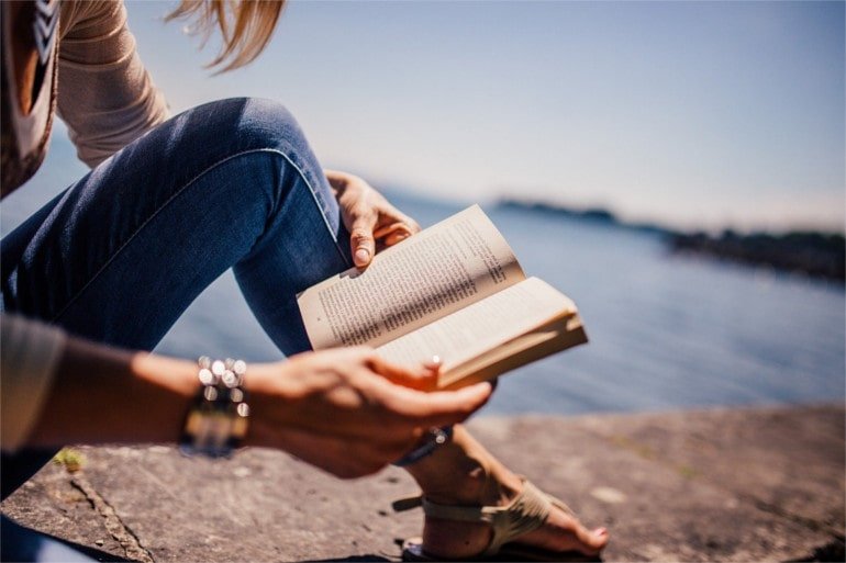 a picture of a girl holding a book near a  sea, with book being an example of a physical prduct